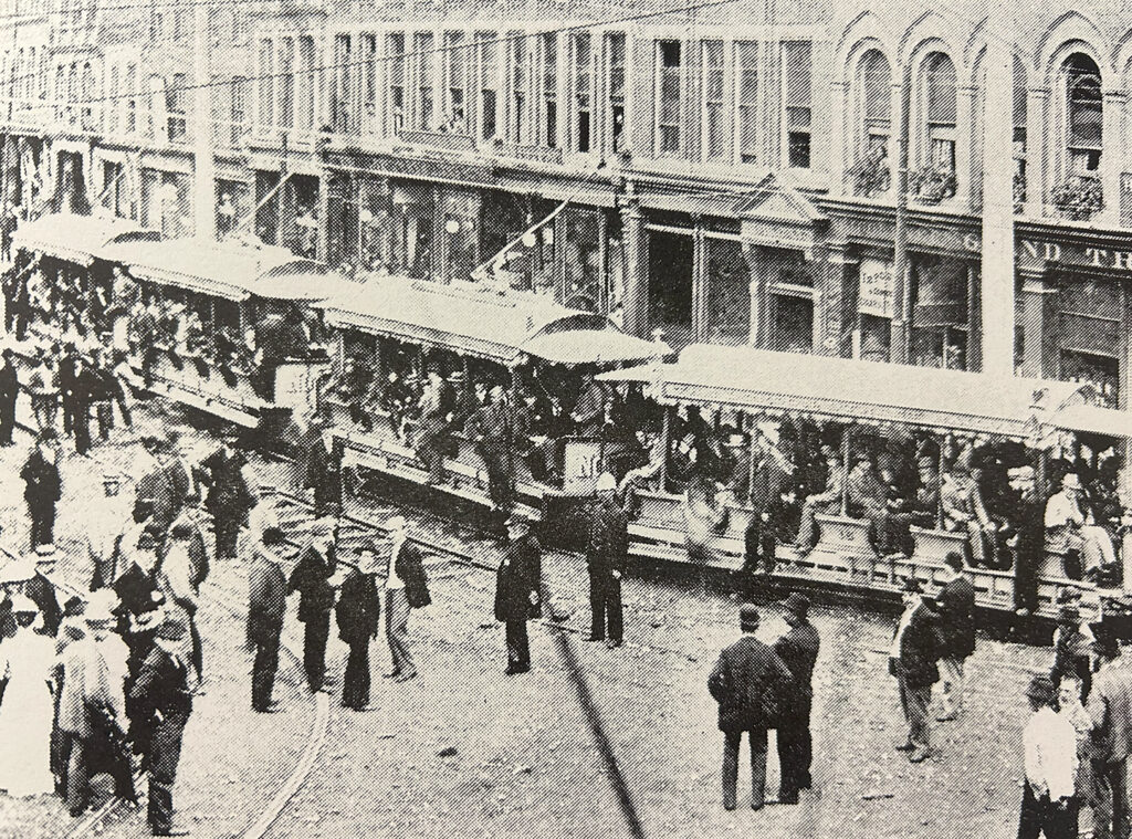 Photo of the LSR streetcar full of riders and pedestrians walking around Downtown London, Ontario from 1885.